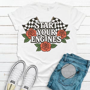 May include: White t-shirt with a black and white checkered flag design and red roses. The text "Start Your Engines" is printed on the shirt.