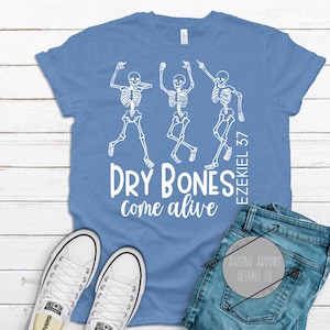 May include: A light blue t-shirt with a white graphic of three skeletons dancing. The text "DRY BONES come alive" and "EZEKIEL 37" are also printed on the shirt.