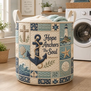 Könnte beinhalten: Ein zylindrischer Wäschekorb aus Stoff mit gestepptem Patchwork-Design in Blau-, Creme- und Beigetönen. Die Vorderseite zeigt einen großen dunkelblauen Anker, einen Leuchtturm, ein Kreuz und den Text Hope Anchors the Soul Hebrews 6:19 mit Seilgriffen.