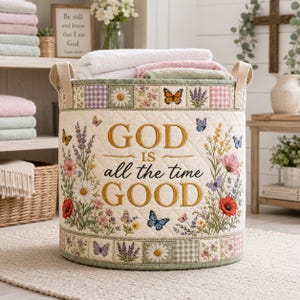 Könnte beinhalten: Ein gesteppter Aufbewahrungskorb aus cremefarbenem Stoff mit Blumen- und Schmetterlingsdruck. Der Text "GOD IS all the time GOOD" ist in Gold und Schwarz gestickt. Der Korb hat einen Patchwork-Rand mit Gänseblümchen, Lavendel und Vichy-Karomustern.