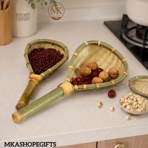 May include: Two bamboo strainers with long handles and woven mesh baskets. The smaller strainer holds dark red beans, while the larger one contains walnuts and red dates. The bamboo frames are secured with light-coloured rattan bindings.