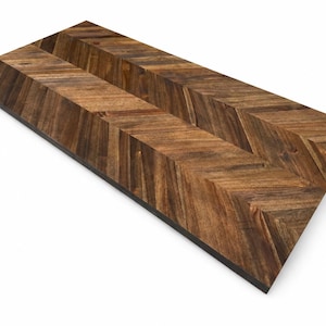 May include: A rectangular wooden board featuring a dark brown chevron pattern. The surface displays natural wood grain variations with alternating light and dark brown tones arranged in a V-shaped design across the entire flat top surface.