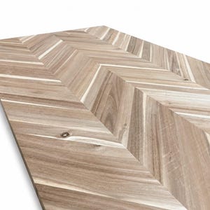 May include: A rectangular wooden panel featuring a light brown and tan herringbone pattern. The surface displays natural wood grain variations, including visible knots and linear textures arranged in a repeating V-shaped chevron design.