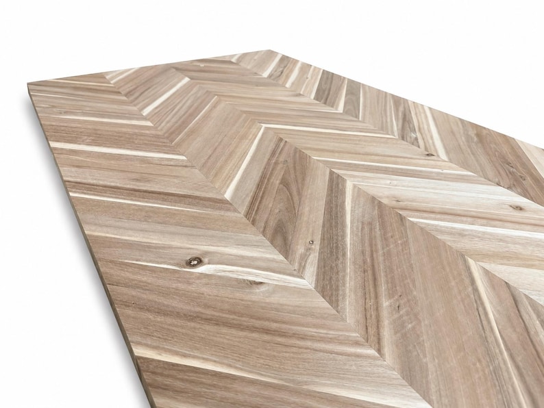 May include: A rectangular wooden panel featuring a light brown and tan herringbone pattern. The surface displays natural wood grain variations, including visible knots and linear textures arranged in a repeating V-shaped chevron design.