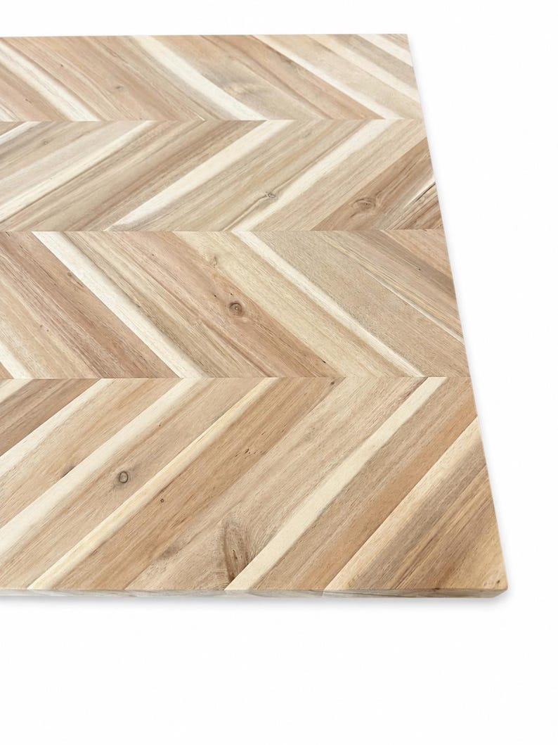 May include: A rectangular wooden board featuring a light brown natural wood grain with a distinct chevron pattern. The surface is composed of multiple angled wooden slats joined together, showcasing variations in color and texture throughout.