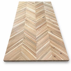 May include: A rectangular wooden tabletop featuring a light brown natural wood grain with a distinct chevron pattern. The surface is composed of multiple planks arranged in a V-shaped design, showcasing varied wood tones and textures.