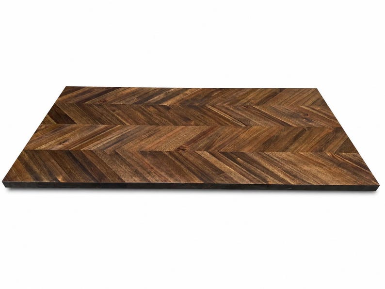 May include: A rectangular wooden tabletop featuring a dark brown finish and a prominent herringbone pattern. The surface displays natural wood grain variations with alternating light and dark brown tones arranged in a repeating chevron design.