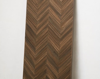 May include: A tall, rectangular wooden panel featuring a dark brown finish with a prominent herringbone pattern. The wood grain is visible throughout the surface, and the panel is framed by a thin, matching dark brown border along its edges.