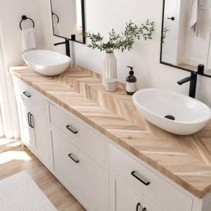 May include: A double bathroom vanity featuring a light wood countertop with a herringbone pattern, two white oval vessel sinks, and matte black hardware. The vanity includes white cabinets with drawers and doors, paired with two black-framed mirrors.