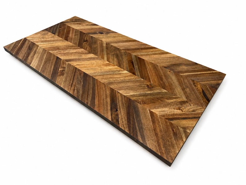 May include: A rectangular wooden board featuring a prominent chevron pattern. The surface displays a mix of light and dark brown wood grain tones, arranged in a V-shaped orientation that runs the length of the board, creating a textured appearance.