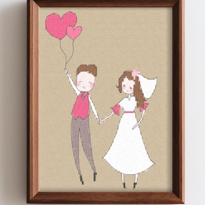 Peut inclure: Une broderie au point de croix encadrée représentant deux personnages se tenant par la main. L'un porte un gilet rose et un pantalon gris, tenant deux ballons en forme de cœur rose. L'autre porte une robe blanche et un voile de mariée.