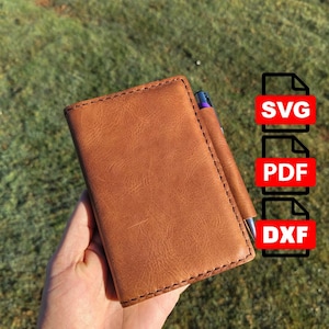 May include: A tan leather notebook cover with visible stitching along the edges and a built-in pen loop holding a silver pen. To the right, three red rectangular icons display the white text SVG, PDF, and DXF respectively.