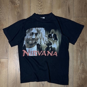 Puede incluir: Una camiseta negra de manga corta con un estampado gráfico de la banda Nirvana. El diseño incluye un gran retrato de Kurt Cobain a la izquierda, dos imágenes de actuaciones más pequeñas a la derecha y la palabra NIRVANA en texto rojo debajo.