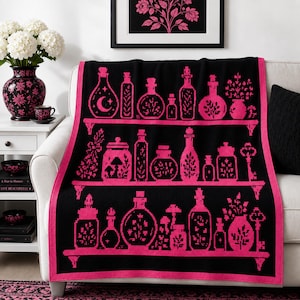 May include: A black and hot pink knit throw blanket featuring a repeating pattern of shelves filled with various glass bottles, jars, and keys. The design includes botanical elements and a crescent moon motif, finished with a solid pink border.