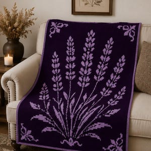 Puede incluir: Una manta de ganchillo rectangular con una base de color morado intenso y un patrón de flores de lavanda pixeladas en color lavanda claro. La manta tiene un borde a juego y motivos decorativos en las esquinas con textura uniforme.