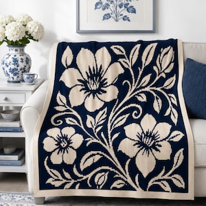 May include: A rectangular knit throw blanket featuring a dark navy blue background with a large-scale cream-colored floral pattern of blooming flowers and leafy vines. The blanket is finished with a solid cream-colored border along all four edges.