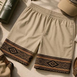 Puede incluir: Pantalones cortos de color beige con cintura elástica y un patrón geométrico marrón oscuro a lo largo del dobladillo. Los pantalones se muestran junto a una botella de agua verde, gafas de sol, una gorra beige con parche Timber Raw, una camisa y sandalias.