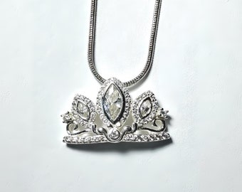 May include: A silver necklace with a crown pendant featuring clear cubic zirconia stones.