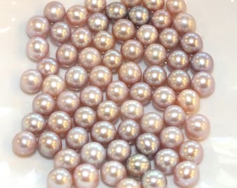 May include: A collection of round, iridescent pearls in shades of pink, lavender, and grey. The pearls are arranged in a random pattern on a white surface.