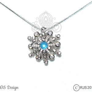 May include: Silver snowflake necklace with a light blue crystal centre. The snowflake is surrounded by smaller clear crystals.