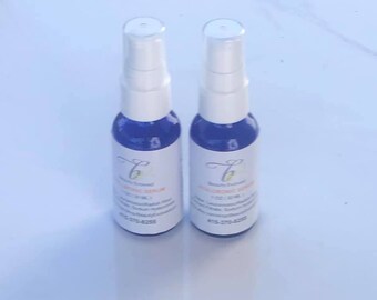 May include: Two blue bottles of hyaluronic acid serum with white pump tops and white labels. The labels have the text "Beauty Essence" and "Hyaluronic Serum" in a cursive font.