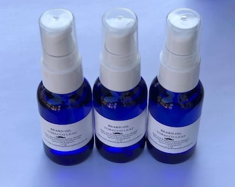 May include: Three blue glass bottles with white pump tops and labels that read "Beard Oil Tobacco Leaf". The bottles are on a white surface.