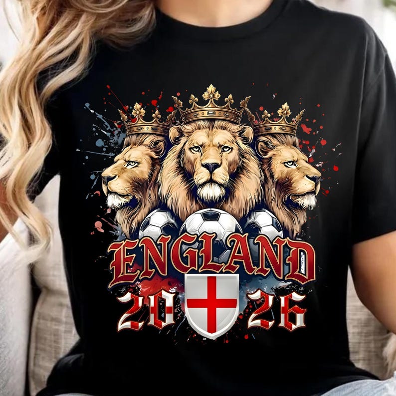 May include: A black t-shirt featuring a graphic of three lions wearing crowns above three soccer balls. The text "ENGLAND" appears in red lettering above a shield displaying the St. George's Cross, flanked by the numbers "20" and "26" in red.