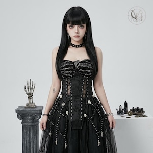 May include: A black strapless corset dress featuring a ribcage graphic on the bodice, a central heart-shaped embellishment, and a skirt adorned with small skull accents, lace-up side panels, and dangling silver-toned chain details throughout.