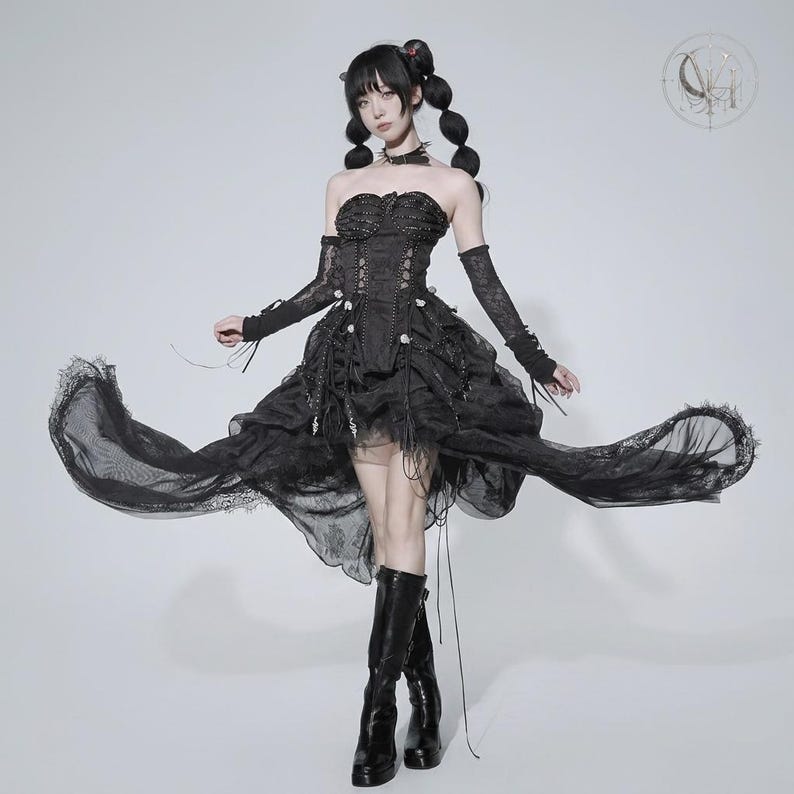 May include: A black strapless corset dress featuring a layered, high-low skirt with lace trim, paired with matching lace arm warmers and a choker. The bodice includes vertical boning and decorative lacing, while the skirt has a ruffled, voluminous silhouette.