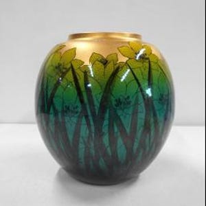 Può includere: Un vaso rotondo in ceramica caratterizzato da una sfumatura di colore che passa da una base verde acqua scuro a un centro verde brillante e un bordo dorato. La superficie è decorata con un motivo scuro a silhouette di fili d'erba alti.