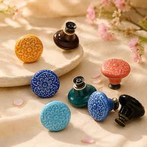 Può includere: Una collezione di pomelli rotondi in ceramica per mobili con motivi floreali in rilievo in vari colori, tra cui giallo, blu, azzurro, verde acqua, corallo e nero. Ogni pomello ha una base metallica e una finitura lucida sulla superficie.