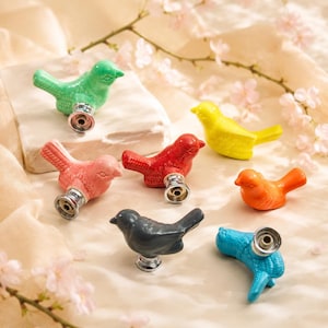 May include: A collection of seven ceramic bird-shaped drawer knobs in various colors including mint green, light pink, red, yellow, orange, dark gray, and bright blue. Each knob features a metallic silver-toned base for mounting to furniture.