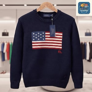 Peut inclure: Un pull en tricot bleu marine à manches longues orné d'un motif de drapeau américain sur la poitrine. Le motif du drapeau présente des étoiles blanches sur un fond bleu avec des rayures rouges et blanches. Les lettres RL sont brodées en rouge.