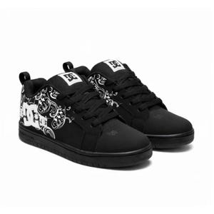 May include: A pair of black low-top trainers featuring a white DC logo on the tongue and side. The side panels display a white intricate paisley-inspired graphic pattern. The shoes have black laces, a padded collar, and a solid black rubber sole.