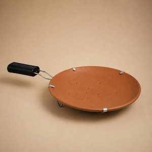 May include: A round, flat, terracotta-colored cooking pan with a smooth surface and small perforations. It features a black rectangular handle attached by a metal frame, with four silver-colored metal clips securing the pan to the frame.