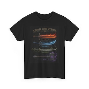 Puede incluir: Una camiseta negra de manga corta con un gráfico que incluye el texto CHOOSE YOUR WEAPON. El diseño muestra cuatro armas etiquetadas con lenguajes de programación: una espada C++ en llamas, una hoja Golang azul brillante, una katana Python y un martillo Rust.