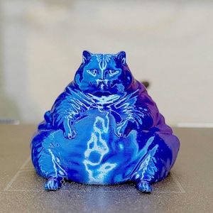May include: A 3D printed figurine of a rotund cat with a glossy, deep blue finish. The cat is depicted in a seated, upright position with a prominent, rounded belly, pointed ears, and visible facial features, showcasing a smooth, reflective surface.