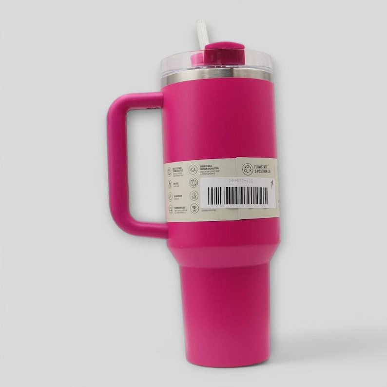 May include: A bright pink insulated tumbler with a large side handle and a clear lid featuring a white straw. A rectangular product label is wrapped around the center, displaying technical specifications, a barcode, and the text Flowstate 3-Position Lid.