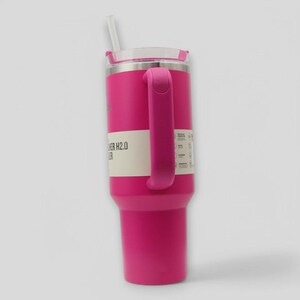 May include: A bright pink insulated tumbler with a matching side handle, a clear lid, and a white straw. A paper band wraps around the center, featuring the text "FLOWSTATE TUMBLER H2.0" and "STANLEY" along with various product feature icons.