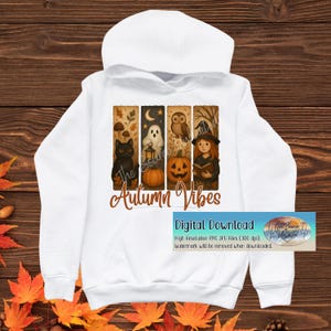 Könnte beinhalten: Weißer Kapuzenpullover mit einer farbenfrohen Grafik mit herbstlichen Illustrationen: einer schwarzen Katze, einem Geist, einer Eule, einem Kürbis und einer Hexe. Der Text "Autumn Vibes" wird darunter angezeigt. Der Hoodie hat auch ein Digital-Download-Banner.