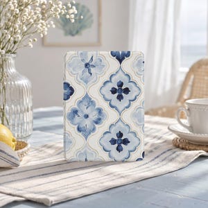 May include: A rectangular e-reader case featuring a repeating pattern of blue and white quatrefoil floral motifs. The design consists of stylised dark blue and light blue flower shapes set against a cream background with thin gold outlines.