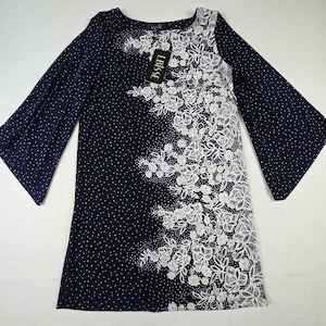 May include: A navy blue tunic dress featuring a white polka dot pattern across the fabric. The right side displays a large, intricate white floral lace overlay. The garment has wide, flared sleeves and a black brand tag labeled LBISSE.
