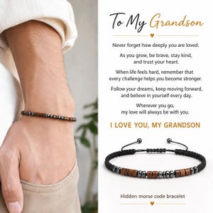 Könnte beinhalten: Ein Morsecode-Armband mit abwechselnden braunen Holzperlen und metallisch grauen Perlen an einer schwarzen Kordel. Die beiliegende Karte zeigt den Text: To My Grandson, Never forget how deeply you are loved. As you grow, be brave, stay kind, and trust your heart. I LOVE YOU, MY GRANDSON.