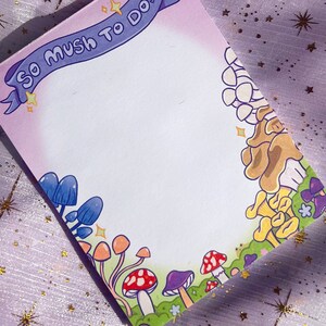 May include: A pink and purple notepad with a blue ribbon that says "So much to do!"  The notepad is decorated with a border of colorful mushrooms.