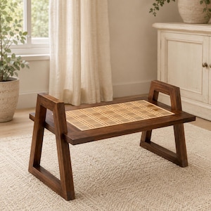 Puede incluir: Una mesa baja rectangular de madera con acabado marrón oscuro y patas inclinadas. El tablero presenta una incrustación central con un patrón de cuadros en color tostado claro y marrón. La estructura incluye dos soportes laterales verticales.