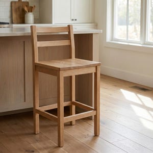 Può includere: Uno sgabello da bar in legno chiaro con seduta quadrata, uno schienale a pioli con due listelli orizzontali e quattro gambe dritte collegate da un poggiapiedi su tutti i lati. Lo sgabello è realizzato in legno naturale con venature visibili.