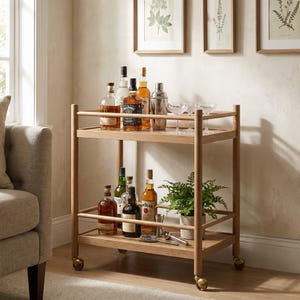 May include: A light wood bar cart with two rectangular shelves and four caster wheels. The top shelf holds various glass liquor bottles, a metal cocktail shaker, and two stemmed glasses. The bottom shelf holds more liquor bottles, a potted fern, and metal bar tools.