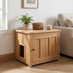 May include: A light oak wood pet enclosure cabinet featuring a rectangular top, a single door with a small black knob, and a side cutout entry. The cabinet is topped with a green potted fern, a woven basket, and a cylindrical candle in a glass jar.