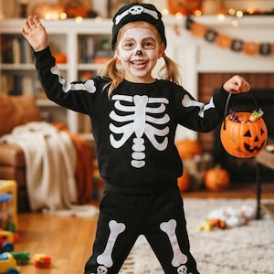 May include: A black long-sleeved sweatshirt and matching pants featuring a white skeleton bone print, paired with a black beanie with a skull graphic. The text "Last-Minute Halloween Costume!" is displayed at the top of the image.