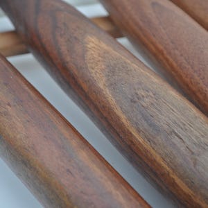 May include: Close-up of several wooden rolling pins with a rich, dark brown finish. The rolling pins are arranged parallel to each other, showcasing the natural wood grain and texture. The image highlights the craftsmanship of the kitchen tools.